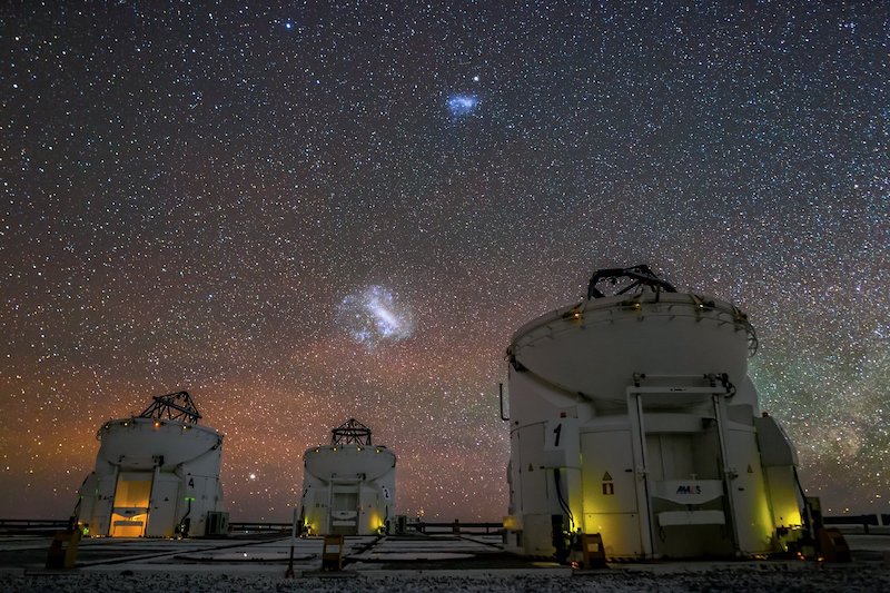 Két szabálytalan izzó homályos folt az égen több nagy teleszkópkupola felett.