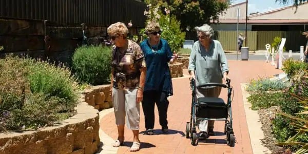 3 idős néni sétál az utcén egyiknél kerekes kis tili toli van amire le lehet ülni. Közös séta segít a szorongáson